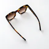 Lentes de sol Duna con armazón de policarbonato color beige y diseño rectangular con esquinas levemente angulares. Lentes oscuros con filtro UV400 y patillas gruesas.