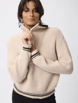 Sweater de tejido grueso en color beige, con cuello alto y cierre frontal parcial. Presenta detalles de rayas negras en contraste en el borde del cuello y en los puños.