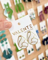 Caravanas de diseño tipo gota con acabado esmaltado en color blanco y bordes dorados, presentando un patrón interno texturizado.