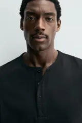 Camiseta blanca de manga corta con cuello redondo y tapeta de botones frontal (cuello panadero o henley).