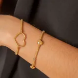 Pulsera de malla metálica con dije central en forma de corazón, ambos en acabado dorado.
