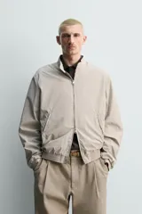 Cazadora regular fit de tejido técnico color beige, con cuello subido, cierre de botones y cremallera frontal, bolsillos de doble vivo en la cadera y acabados elásticos.
