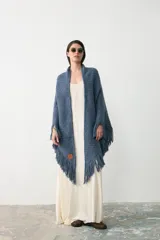 Ruana triangular tejida en lana merino extrafina, lino y viscosa, con textura aireada y terminación de flecos en los bordes. Diseño versátil y envolvente.