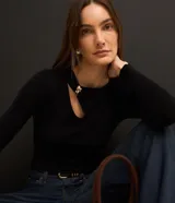 Blusa negra de punto acanalado, con mangas largas, cuello redondo con detalle metálico dorado y abertura asimétrica en el hombro.