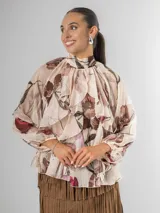 Camisa de seda italiana con estampado floral en tonos rosados, marrones y verdes. Presenta cuello alto con volados que caen en cascada sobre el frente y mangas largas abullonadas con puños ajustados.