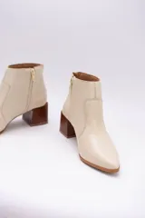 Botas cortas de cuero color beige, con punta fina y cierre lateral. Tienen un taco cuadrado de madera.