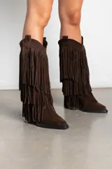 Botas texanas de gamuza color marrón, con diseño de caña alta adornada con múltiples capas de flecos. Presentan taco cuadrado y punta ligeramente afinada.