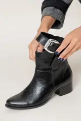 Bota corta de cuero color chocolate, con taco cuadrado y hebilla metálica decorativa en el lateral. Presenta un diseño clásico con punta redondeada.