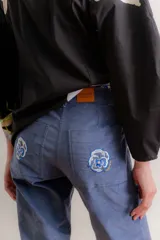 Pantalón de corte recto tipo jean, confeccionado en pana elastizada color azul grisáceo. Presenta bolsillos traseros con detalles bordados florales.