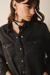 Camisa de estilo tejano en color negro lavado, con cuello camisero, cierre frontal con botones metálicos y dos bolsillos delanteros con solapa.