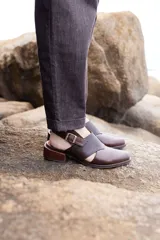 Zapato destalonado de cuero marrón con puntera cerrada, detalles de textura grabada en la capellada y tira ajustable con hebilla en el talón, con taco bajo y ancho.