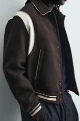 Cazadora estilo varsity de corte cropped, confeccionada en tejido de lana marrón con mangas en contraste color crema. Presenta cuello solapa, cierre frontal con botones a presión, bolsillos laterales de vivo y acabados en rib a rayas en puños y cintura.