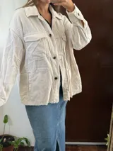 Campera de pana color blanco marfil, con bolsillos frontales con solapa, bolsillos laterales ojetes, cierre con botones oscuros y detalles de terminaciones deshilachadas.