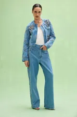 Pantalon de denim azul con corte recto y amplio, decorado con detalles de pedrería y bordados en los laterales que forman un patrón de rombos.