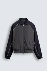 Cazadora relaxed fit en color block, con cuerpo gris oscuro y mangas azul marino. Presenta cuello subido, manga larga, bolsillos frontales de vivo, vivos combinados a contraste en blanco, acabados con rib elástico y cierre frontal con cremallera.