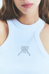 Musculosa de morley color blanco, con cuello alto y diseño de espalda nadadora. Presenta un isologo frontal bordado con tachas brillantes.