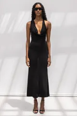 Vestido largo negro de corte al cuerpo, con escote halter y cuello drapeado. Presenta una silueta entallada que se ensancha suavemente hacia el ruedo.