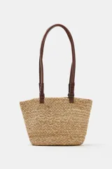 Bolso tipo shopper formato mini confeccionado en yute trenzado, con doble asa de mano en cuero sintético color marrón.