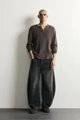 Jeans de denim de algodón color gris con efecto lavado, de corte relaxed barrel fit y tiro medio. Presenta diseño amplio con pinzas en las rodillas y costuras curvas, cierre frontal con botones y cinco bolsillos tradicionales.