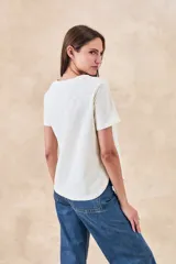 Remera de algodón color blanco con bordados florales y geométricos en color negro. Presenta cuello redondo, mangas cortas y un diseño con franjas horizontales bordadas.