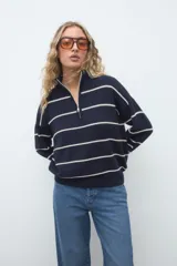 Sweater de punto azul marino con rayas horizontales blancas, cuello alto con cierre frontal y manga larga de diseño holgado.