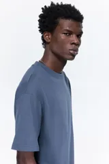 Remera de algodón de peso medio, color azul, con cuello redondo ribeteado, hombros caídos y corte relajado.
