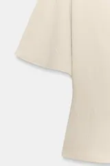Top fluido de color beige con cuello perkins y mangas acampanadas por debajo del codo. Presenta un diseño de bajo redondeado y textura sutil en la tela.