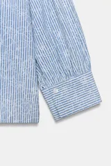 Camisa de cuello solapa y manga larga con puños abotonados. Presenta un diseño de rayas verticales azules y blancas con un estampado floral lineal superpuesto. Cierre frontal con botones.