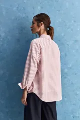 Camisa de calce relajado a rayas rosadas y blancas, con cuello camisero clásico y frente abotonado. Presenta recortes con cambio de dirección en las rayas y silueta amplia.