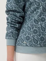 Buzo de algodón orgánico con cuello redondo y mangas largas. Presenta un diseño estampado con motivos florales y paisley en técnica flock sobre fondo gris.