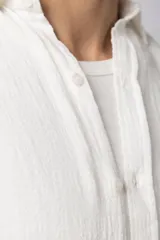 Camisa de lino blanca de manga larga, con cuello clásico y cierre frontal con botones. Corte recto y holgado.