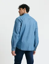 Camisa de jean de manga larga con cuello clásico, cierre frontal con botones y bolsillo tipo parche en el pecho.