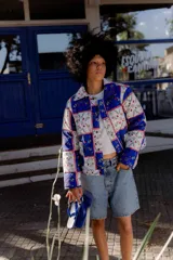 Campera corta con estampado floral en tonos azules, rojos y amarillos sobre fondo blanco. Diseño capitoneado a mano en 100% algodón, con cuello camisero, broches metálicos y bolsillos plaqué.