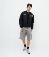 Campera bomber negra de microfibra, con cierre frontal por cremallera, puños y ruedo elásticos, y bolsillos con cierre. Cuenta con múltiples parches y estampas bordadas alusivas a la NASA, incluyendo el logo principal en el pecho, insignias en la manga derecha y una bandera de Estados Unidos.