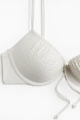 Top de bikini push-up color blanco, con aros, textura gofrada, tirantes finos dobles ajustables y un lazo decorativo en el centro del busto.