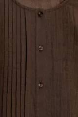 Blusa de cuello redondo y manga sisa con volantes, color marrón, con detalles de entredoses a tono, jaretas delanteras y cierre frontal con botones.