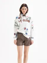 Buzo de silueta holgada y diseño rústico en color blanco, con estampado floral full print y la inscripción "LE CLUB" en el pecho. Cuenta con capucha, ojales metálicos y cordón regulable.