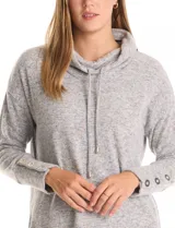 Buzo de tejido suave con cuello volcado ajustable mediante cordones con punteras metálicas. Presenta mangas largas con puños decorados con botones metálicos, hombros caídos y ruedo redondeado con aberturas laterales.