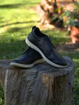 Zapato de estilo casual con cordones, confeccionado en cuero negro con textura granulada, montado sobre una suela de goma blanca de diseño deportivo.