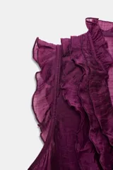 Blusa sin mangas color morado intenso, con escote en V profundo adornado con volantes fruncidos que recorren el frente y el cuello. Presenta cierre frontal con botones pequeños.