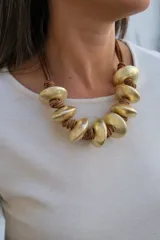 Collar de diseño artesanal compuesto por piezas circulares de metal dorado con acabado mate, intercaladas con nudos de cordón de cuero marrón.