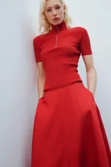 Falda midi de tiro alto y corte en A, color rojo, con bolsillos laterales ocultos y cierre lateral con cremallera.