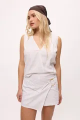 Falda short color crudo, de corte irregular y detalle de arandela dorada.