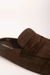 Zueco tipo mocasín destalonado en color verde oliva, con textura grabada efecto cocodrilo y acabado en gamuza.