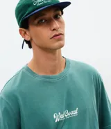 Remera de algodón con efecto lavado gastado, cuello redondo y mangas cortas. Presenta un diseño con estampa frontal localizada con lettering West Coast y un calce levemente suelto.