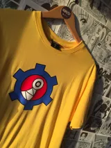 Remera amarilla con estampado de engranaje azul y diseño abstracto en rojo, blanco y negro.