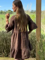 Vestido corto de lino color beige claro, con cuello mao, escote con botones de nácar, mangas tres cuartos con volados y ruedo con volado.