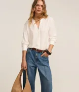 Pantalón wide leg de tiro alto confeccionado en denim de algodón. Presenta un diseño con friso vertical en el frente, cierre de botón y cremallera, trabillas en la cintura y bolsillos funcionales en la parte delantera y trasera.