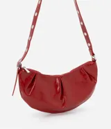 Cartera tipo shoulder bag de diseño media luna, confeccionada en poliuretano con acabado brillante. Presenta detalles frontales estilo gota, cierre superior por cremallera y correa de hombro ajustable con ojetes metálicos.