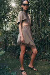 Vestido midi satinado de cuello subido y manga corta tipo capa. Presenta aberturas laterales con aplicación de encaje a tono y bajo asimétrico con detalle de encaje. Incluye un pañuelo integrado en el mismo tejido y cierre posterior con botones forrados.